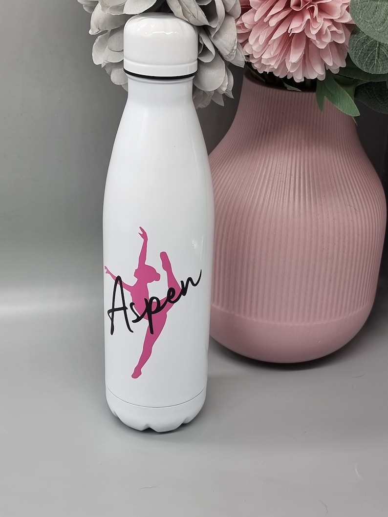 May include: White stainless steel water bottle with a pink silhouette of a dancer and the name "Aspen" in black lettering.