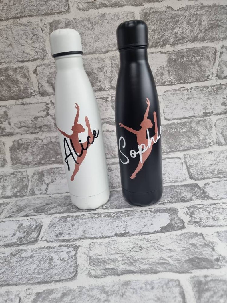 May include: Two personalized water bottles with black and white lids. The bottles have a dancer silhouette with the names "Alice" and "Sophie" printed on them.