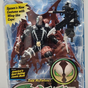 May include: A Spawn II action figure in original blister packaging by McFarlane Toys. The figure features a black costume, skull accents, and a red wing-like cape. It includes a black weapon accessory and text reading Spawn II, Deluxe Edition, and Ages 4 and Up.