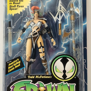 May include: Deluxe Ultra-Action Figure of Angela from Todd McFarlane's Spawn comic book series. The figure is packaged in a blister pack and includes a removable sword and staff that fires a spear. The packaging features the Spawn logo and the text "America's Best Selling Comic Book".