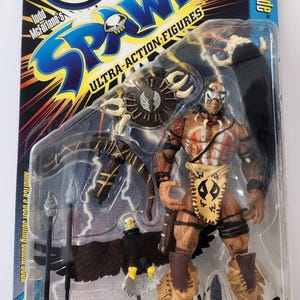 Puede incluir: Figura de acción Spawn Renegade en embalaje original. La figura es marrón y beige con marcas tribales y una máscara. El embalaje presenta el logotipo de Spawn, "Ultra-Action Figures" y "Arrow Fires from Crossbow!"