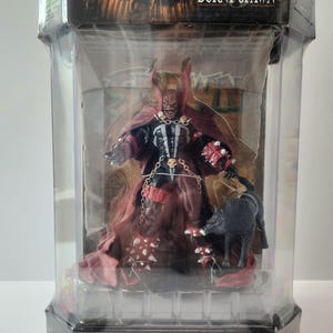 Puede incluir: Figura de acción de Burnt Spawn en una vitrina de plástico transparente. La figura es predominantemente roja y negra, con un diseño detallado. También se incluye una figura de perro negro. El embalaje presenta el texto "BURNT SPAWN" y "SPAWN".