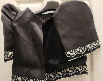 May include: Black satin blouse with puffed sleeves and white embroidered trim. The blouse has a button closure at the neckline.