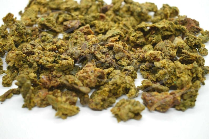 May include: Close-up of a pile of dried, green and brown propolis granules. The granules are irregularly shaped and have a rough texture.