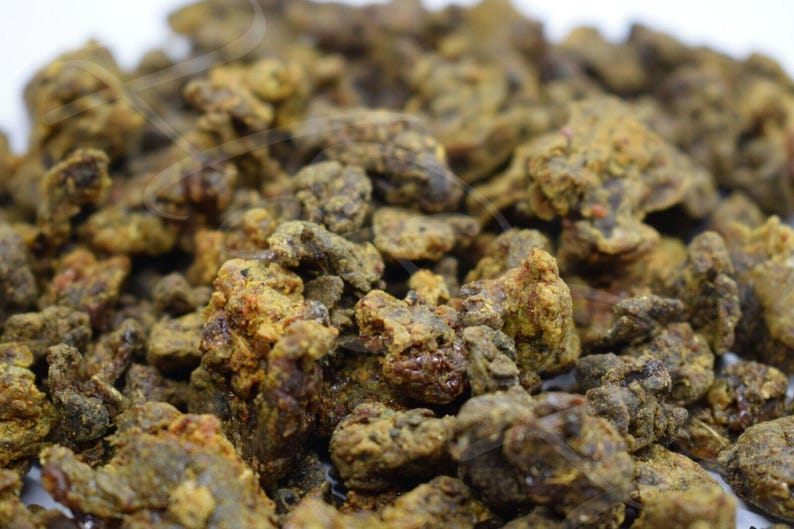 May include: Close-up of a pile of dark brown and yellow propolis resin. The resin is irregularly shaped and has a rough texture.