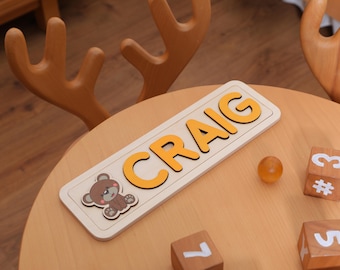 May include: A wooden puzzle with the name CRAIG spelled out in yellow letters. A small brown teddy bear is in the corner of the puzzle.