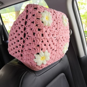 May include: Pink crocheted car seat headrest with white daisy flowers.