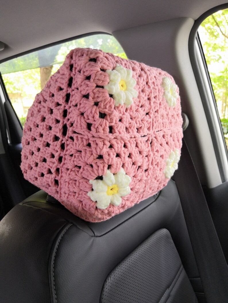 May include: Pink crocheted car seat headrest with white daisy flowers.