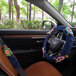 May include: A blue crocheted steering wheel cover with colorful turtle designs. The cover is installed on a car's steering wheel. A matching crocheted turtle design is on the seatbelt.