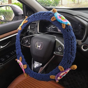 May include: A blue crocheted steering wheel cover with colorful crocheted turtles attached. The cover is on a car steering wheel.