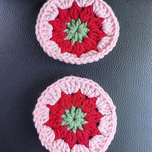 May include: Two crocheted coasters with a pink, red, and green floral design.