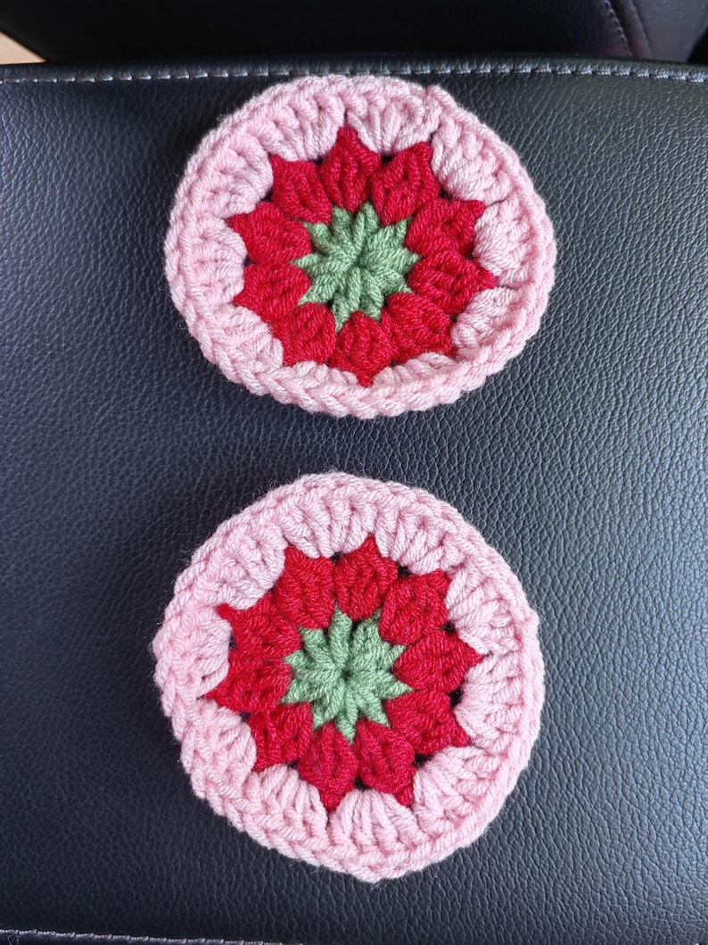 May include: Two crocheted coasters with a pink, red, and green floral design.