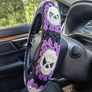 Puede incluir: Cubierta de volante de crochet morado y negro con diseños de calaveras blancas.