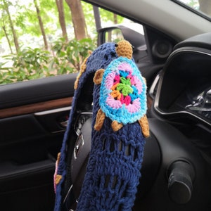 May include: A blue crocheted steering wheel cover with a colorful crocheted turtle design. The turtle has a brown head and legs.