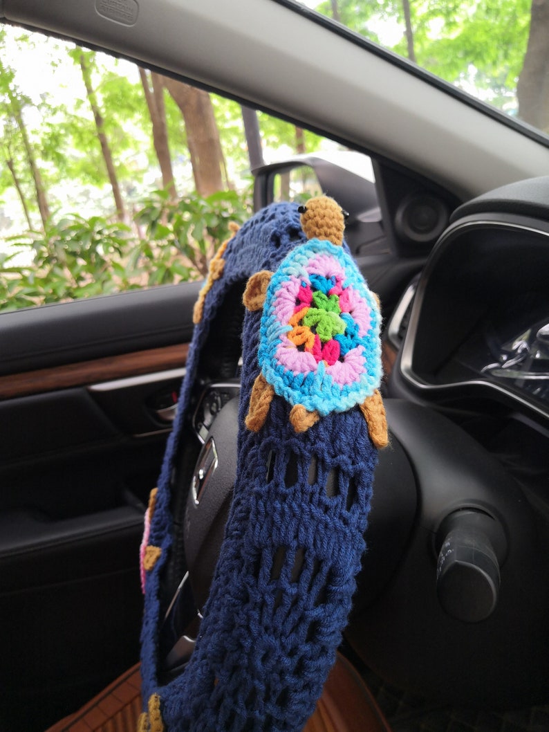 May include: A blue crocheted steering wheel cover with a colorful crocheted turtle design. The turtle has a brown head and legs.