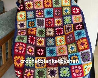 Pode incluir: Uma manta de crochê colorida, feita à mão, com um design de patchwork. A manta apresenta uma variedade de padrões quadrados em tons de vermelho, azul, verde, amarelo e roxo. O texto "crochetblanketbyshan" é visível.