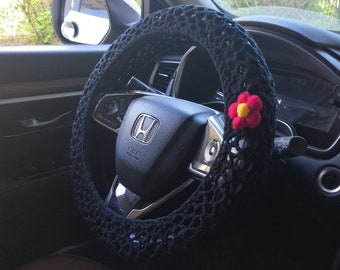May include: Black crochet steering wheel cover with a red and yellow flower accent. The cover is made of a soft, breathable material and is designed to provide a comfortable grip.