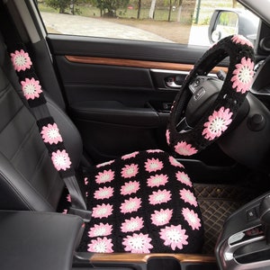 Può includere: Interni di un'auto nera con coprisedili in crochet rosa e nero, una copertura per il volante e una copertura per la cintura di sicurezza.