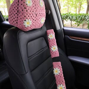May include: Pink crocheted car seat headrest and seatbelt cover with white daisy flowers.