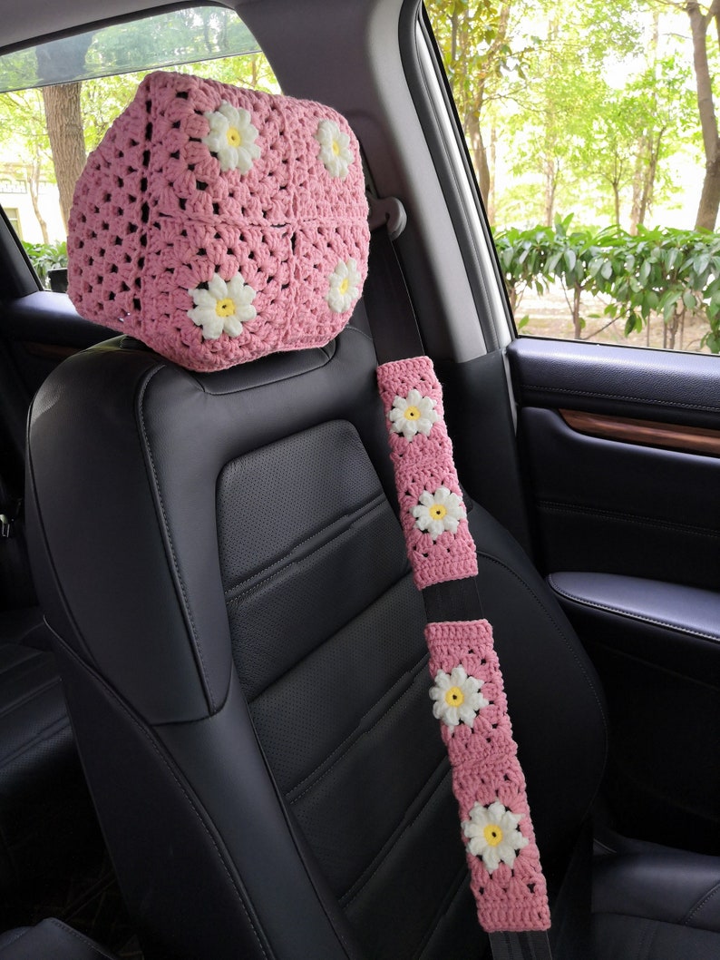 May include: Pink crocheted car seat headrest and seatbelt cover with white daisy flowers.