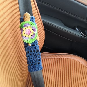 May include: A crocheted turtle seatbelt cover in blue, green, yellow, and pink. The turtle is attached to a black seatbelt.