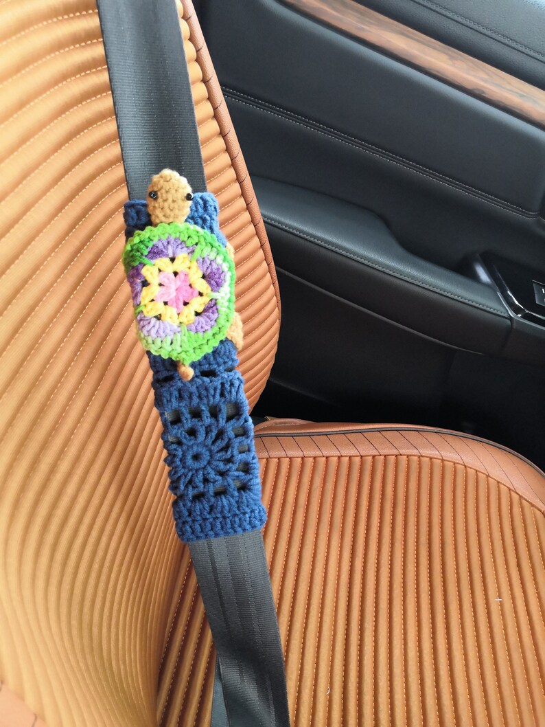 May include: A crocheted turtle seatbelt cover in blue, green, yellow, and pink. The turtle is attached to a black seatbelt.