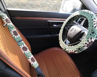 Op de afbeelding: Een groene, witte en bruine gehaakte stuurwielhoes met een bloemenpatroon. De hoes zit op een autostuur met een Honda-logo.