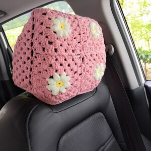 May include: Pink crocheted car seat headrest cover with white daisy flowers.