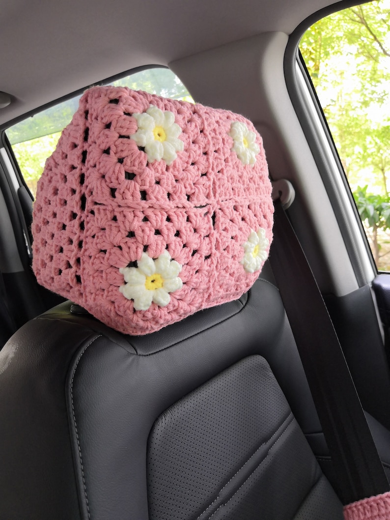 May include: Pink crocheted car seat headrest cover with white daisy flowers.