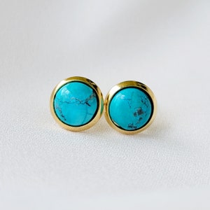 Puede incluir: Un par de pendientes de oro con piedras turquesa. Las piedras son de color azul claro con vetas azules más oscuras.