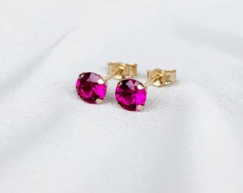 Pode incluir: Um par de brincos de tarracha com pedras redondas facetadas em rosa vibrante, cravadas em metal dourado. Cada brinco possui um design clássico de pino, destacando o corte brilhante das gemas rosas e a cravação em ouro polido.