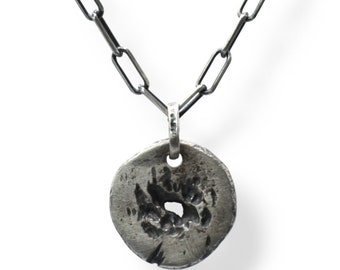 May include: A silver chain necklace with a round pendant featuring a textured, distressed design with a hole in the center.