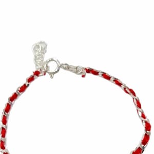 Peut inclure: Un bracelet rouge et argent avec un fermoir argenté. Le bracelet est composé d'un cordon rouge tressé et d'une chaîne argentée.