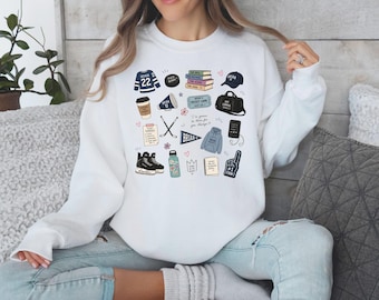 May include: White sweatshirt with various hockey-themed illustrations, including a jersey with the number 22, a hockey puck, books, a hat, a duffel bag, a coffee cup, hockey sticks, ice skates, a water bottle, and a foam finger.