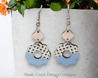 May include: A pair of handmade earrings with a floral design. The earrings feature a light blue and cream color scheme with black polka dots. The earrings are suspended from silver-colored hooks.