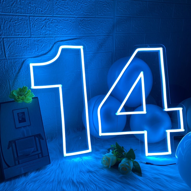 Pu&ograve; includere: Un cartello luminoso al neon a forma di numero 14. Il cartello &egrave; bianco e brilla di blu. Il cartello &egrave; circondato da palloncini blu.