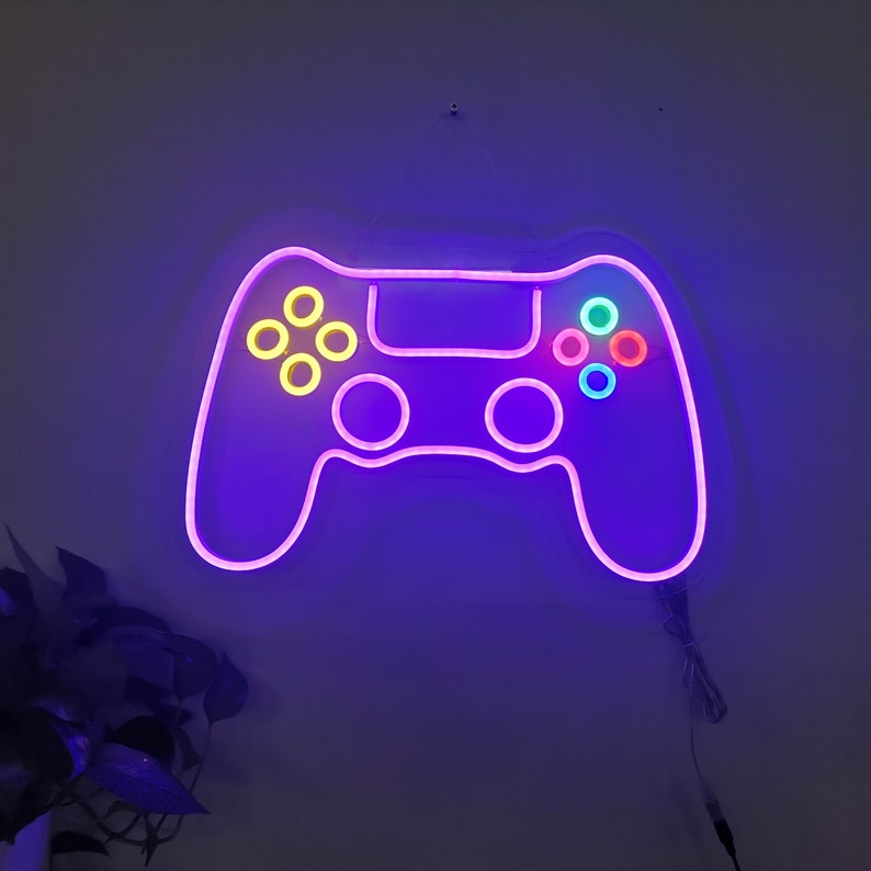 May include: A purple neon light shaped like a video game controller with colorful buttons. The light is mounted on a wall.