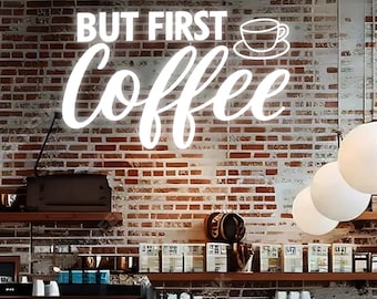 May include: A brick wall with the words "BUT FIRST coffee" in white script. A coffee cup graphic is above the word "coffee". The image is of a coffee shop interior with hanging globe lights.