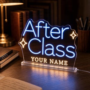 Puede incluir: Un letrero de acrílico transparente con letras de estilo neón azul que dicen After Class y letras blancas que dicen YOUR NAME. El letrero presenta dos iconos de estrellas blancas brillantes a los lados y está montado sobre una base rectangular.