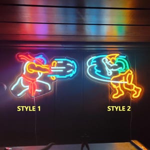 May include: Two neon signs featuring video game character silhouettes. Style 1 shows a figure in red and blue emitting a projectile. Style 2 shows a figure in yellow and blue performing a spinning kick. Both signs are mounted on a dark wall.