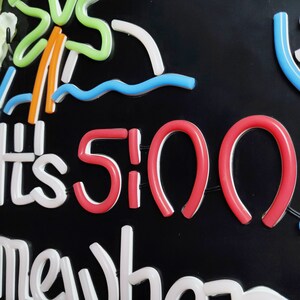 May include: Neon sign with the text "It's 5:00 Somewhere" in white and red. The sign also features a green palm tree, blue waves, and white clouds.