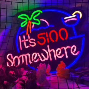 May include: Neon sign with a blue, red and pink colour scheme. The sign reads "It's 5:00 Somewhere" with a palm tree and a cocktail glass graphic.