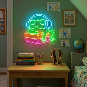 Puede incluir: Un letrero de neón que muestra una rana verde brillante con auriculares azules descansando sobre una pila de libros. La rana está delineada con luz de neón brillante, con los libros iluminados en tonos naranja y rosa sobre una pared.
