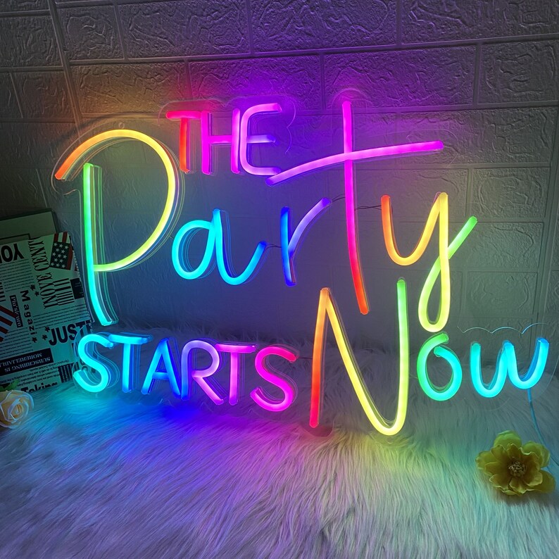 Puede incluir: Un letrero de ne&oacute;n con luces de colores arco&iacute;ris que dice "The Party Starts Now".
