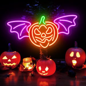 May include: A Halloween-themed display featuring a neon pumpkin with bat wings, glowing in orange, green, and purple. Three carved pumpkins with lit faces and a candle in a jar are arranged on a wooden surface, with leaves and spider decorations.