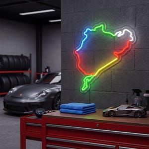 May include: A multi-colored neon sign in the shape of a race track map is mounted on a gray brick wall. A red toolbox with a tire pressure gauge, blue towels, and a model car are on a wooden surface. A gray sports car is in the background.
