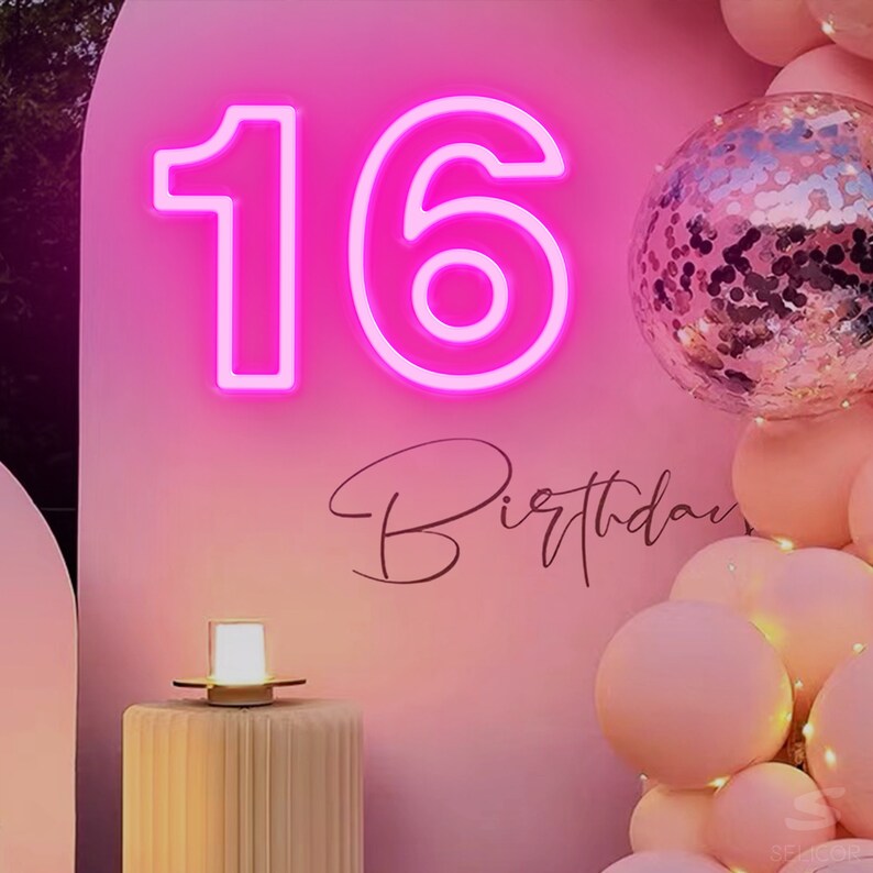 Pu&ograve; includere: Un cartello al neon rosa con il numero 16, circondato da palloncini rosa e bianchi. Il cartello dice "Birthday" in corsivo.