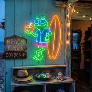 May include: A neon sign featuring a green frog wearing sunglasses and a shirt, holding a drink next to a surfboard. A wooden sign reads BEACH FINDS and ΣΟΥΒΕΝΙΡ. Below, a straw hat, a bowl of sea glass, and an octopus figurine are displayed.