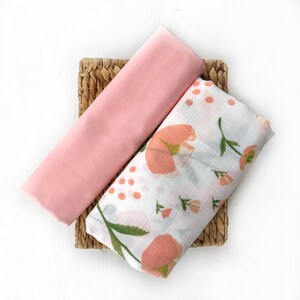 May include: Two pink and white muslin swaddles with a floral pattern. One swaddle is plain pink and the other has a peach floral design.