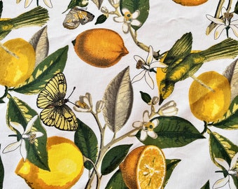 May include: A white fabric with a repeating pattern of lemons, butterflies, and birds. The lemons are yellow with green leaves. The butterflies are yellow and black. The birds are green and yellow.
